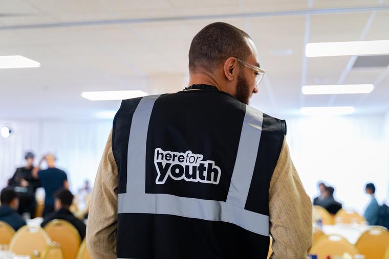 A Here For Youth team member in a branded vest during the evening.